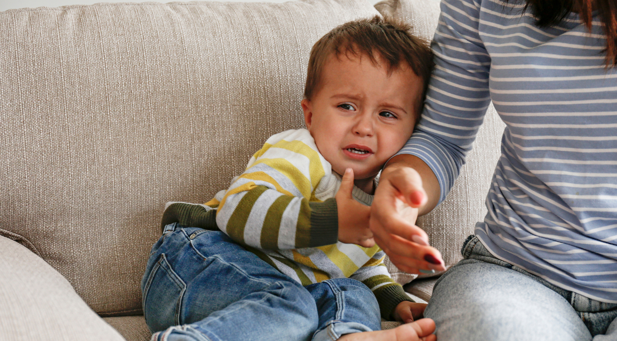 A baby boy crying and tilting his head in his mother's hand