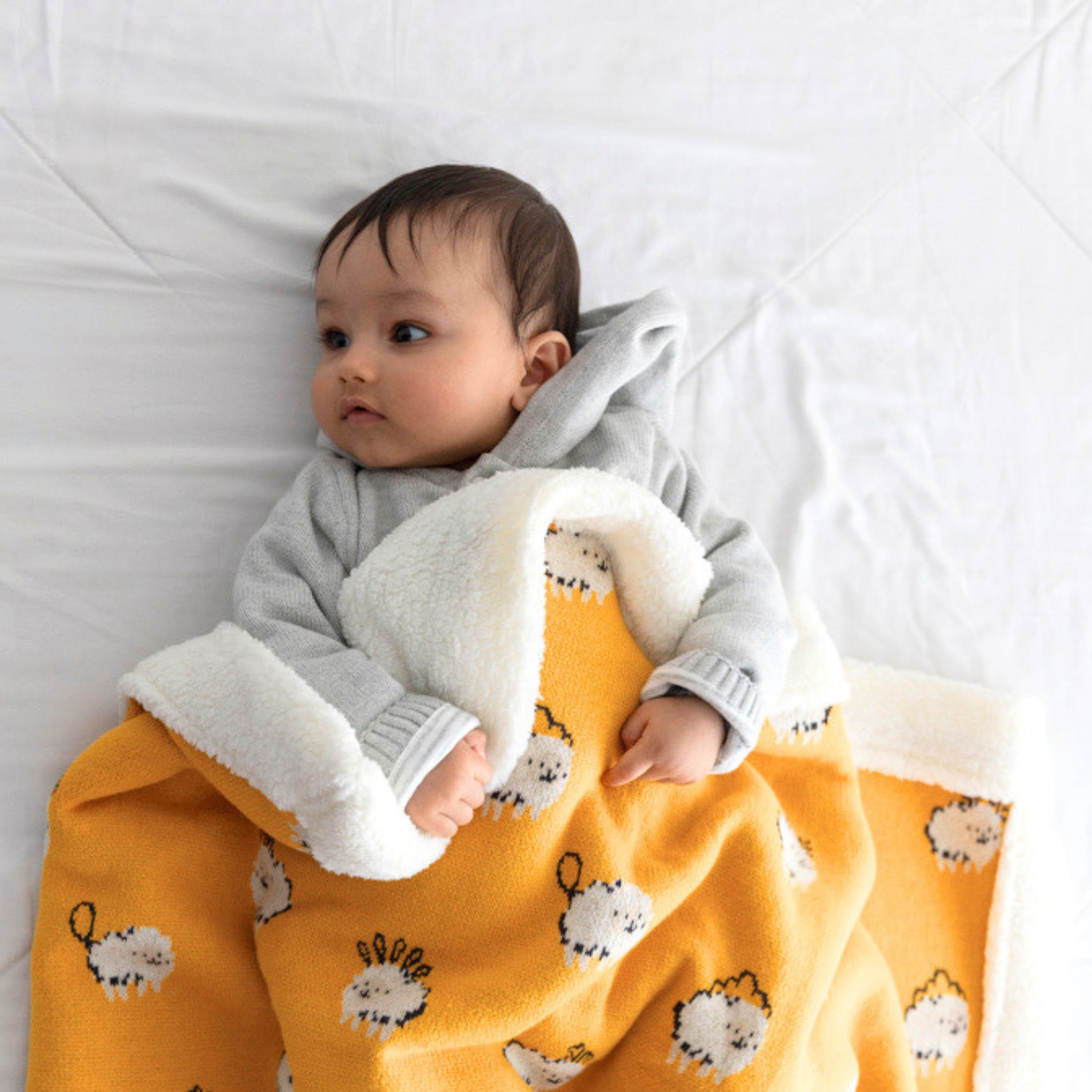 Baby lying in bed & wrapped in a soft yellow fleece blanket with sheep, showcasing cozy warmth and comfort.