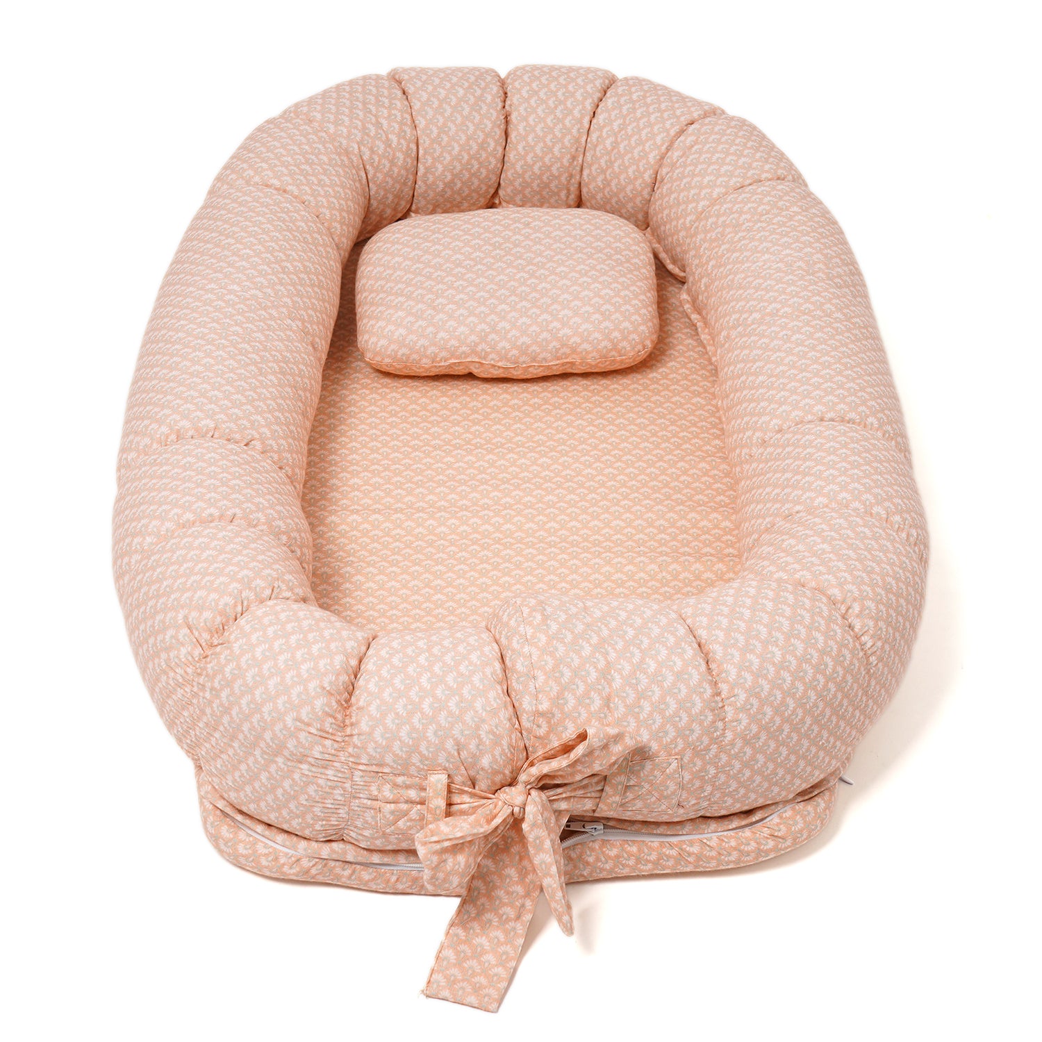 A peach-colored baby lounger with a soft, quilted pattern, featuring a padded oval shape and an attached pillow.