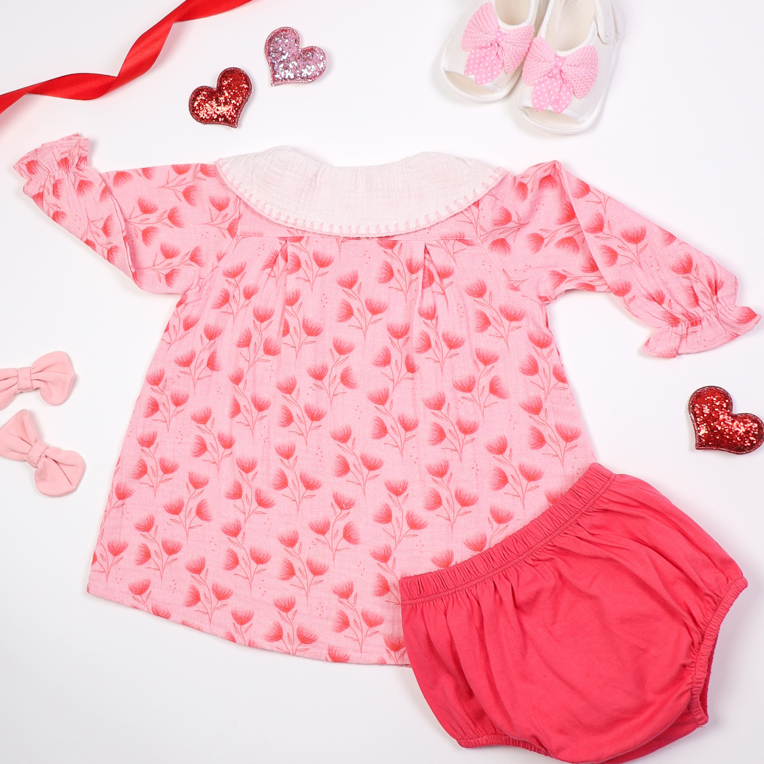 Back view of pink floral baby dress with a large white collar and matching bloomers, displayed on a white background with decorative elements like bows, hearts, and baby shoes.