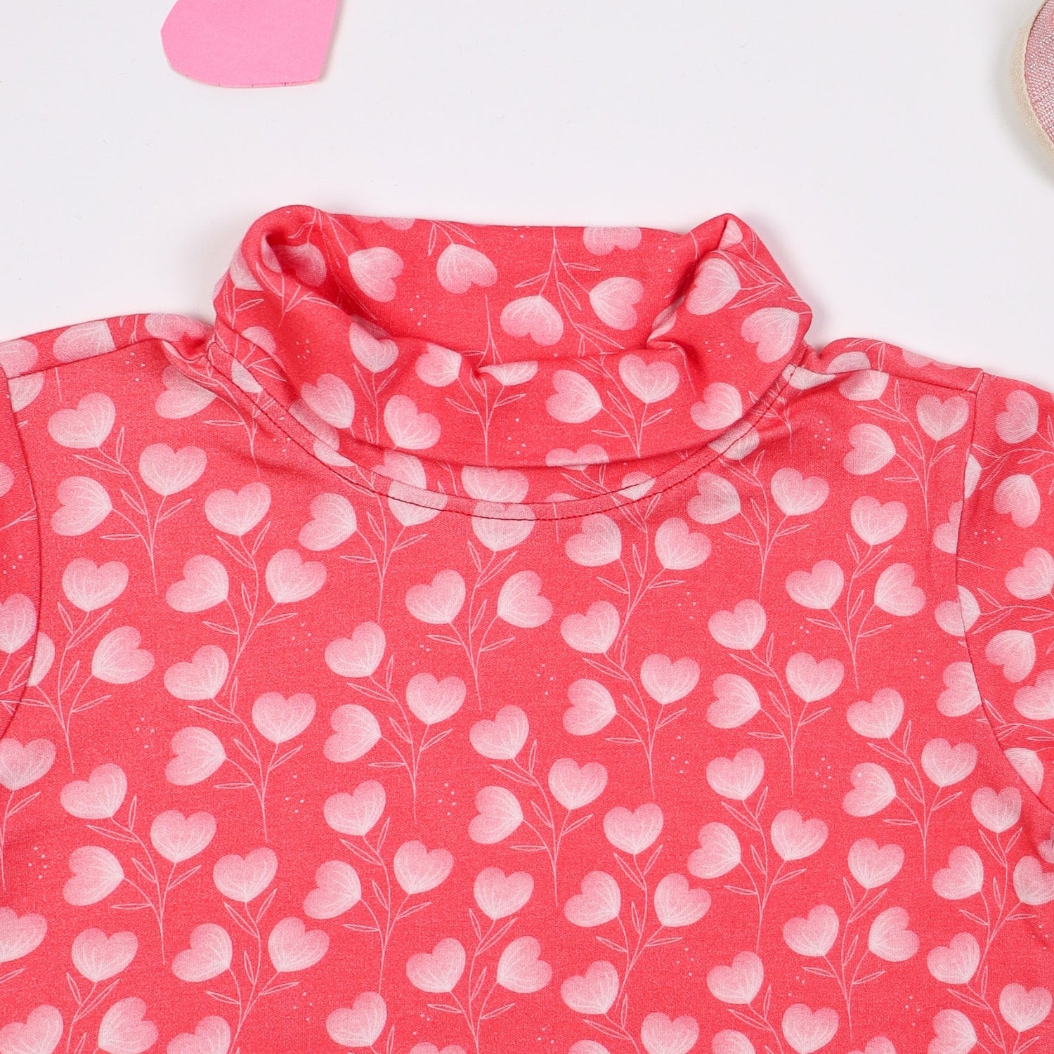 Closeup view of Pink turtleneck long-sleeve top with a heart print, displayed on a white background 