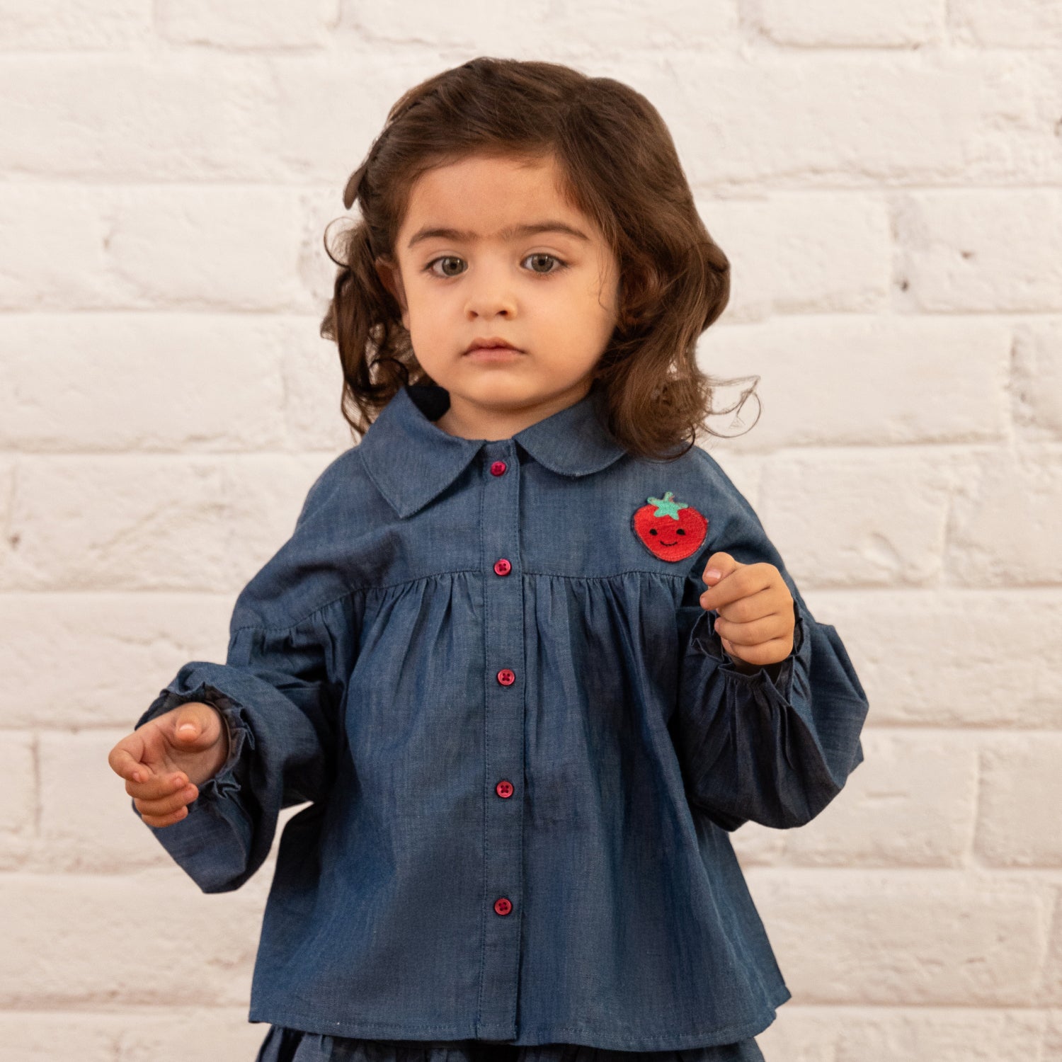 A baby girl is dressed in a Stylish Button Down Strawberry Shirt