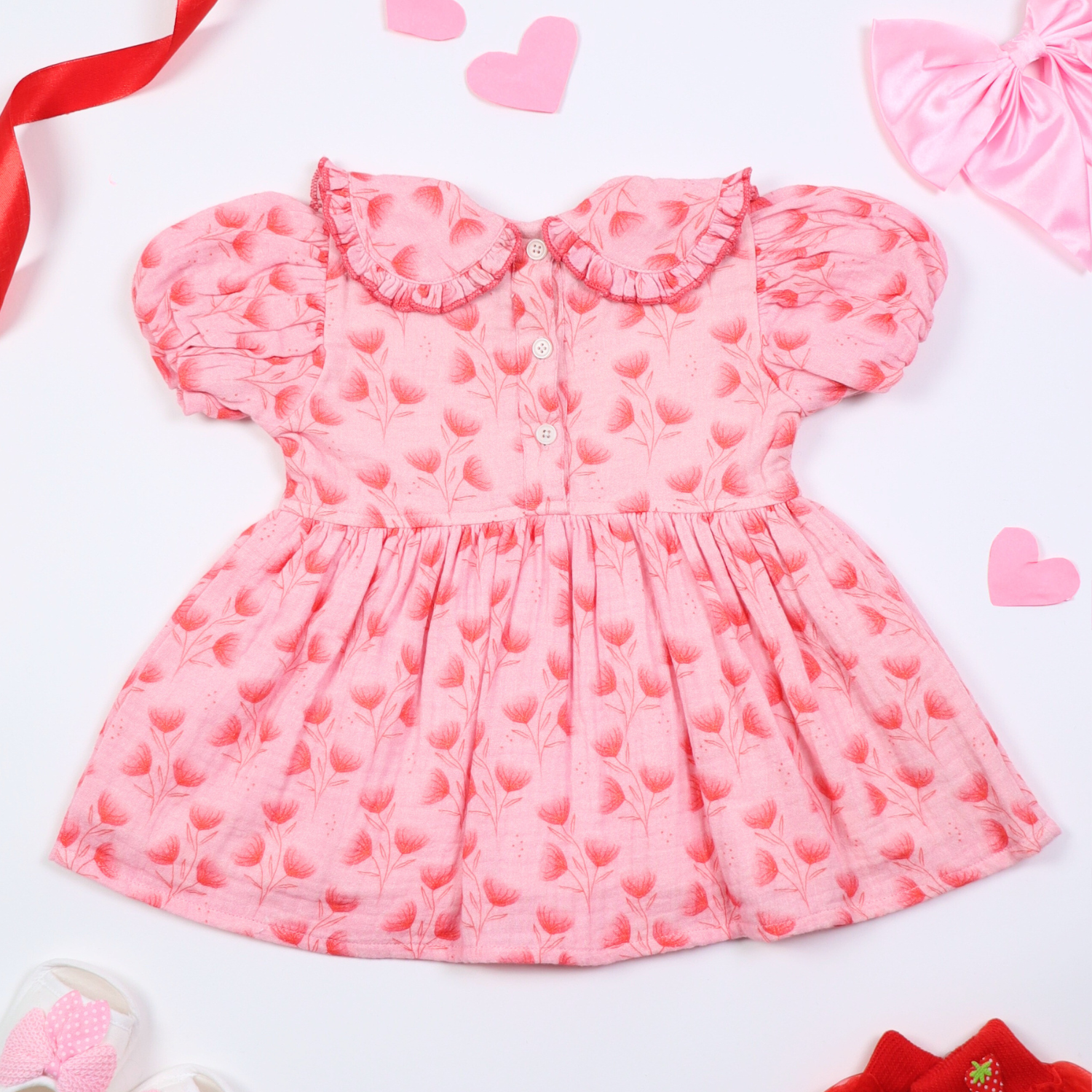 Back view of pink floral baby dress with puff sleeves and a ruffled collar, displayed on a white background with decorative elements like ribbons, hearts, and baby shoes.